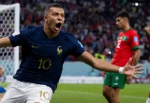 França mira o troféu mundial Mbappé comemora um gol contra Marrocos diante da baliza, com jogadores marroquinos ao fundo.