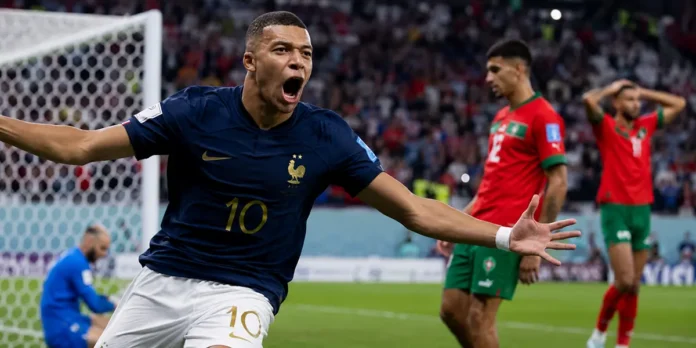 Mbappé comemora um gol contra Marrocos diante da baliza, com jogadores marroquinos ao fundo.